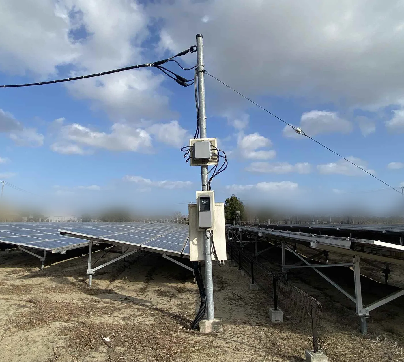 ケーブル盗難の被害を受けた太陽光発電所の引込柱。柱に計器箱と接続箱が取り付けられ、周囲に太陽光パネルの架台が並ぶ。背景は場所の特定を避けるためぼかしている。